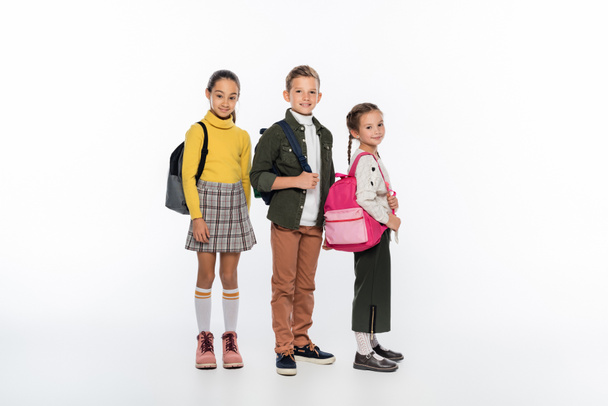 cheerful schoolboy and schoolgirls standing with backpacks on white  - Fotó, kép