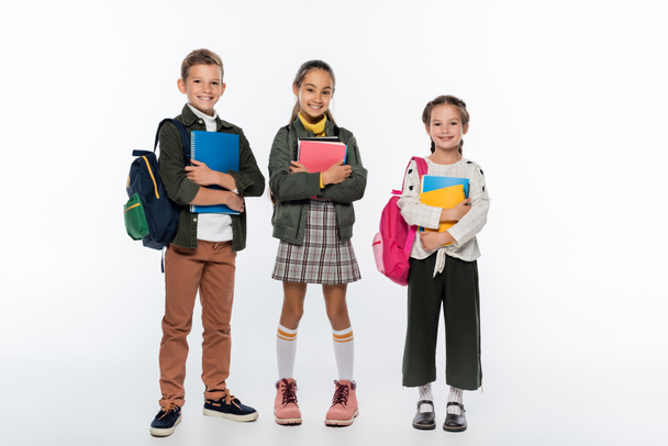 vrolijke schooljongen en schoolmeisjes staan met rugzakken en notitieboekjes op wit  - Foto, afbeelding