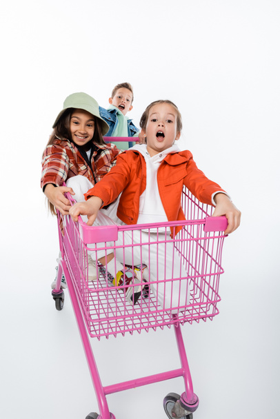 cheerful kids riding in pink shopping cart isolated on white  - Foto, afbeelding