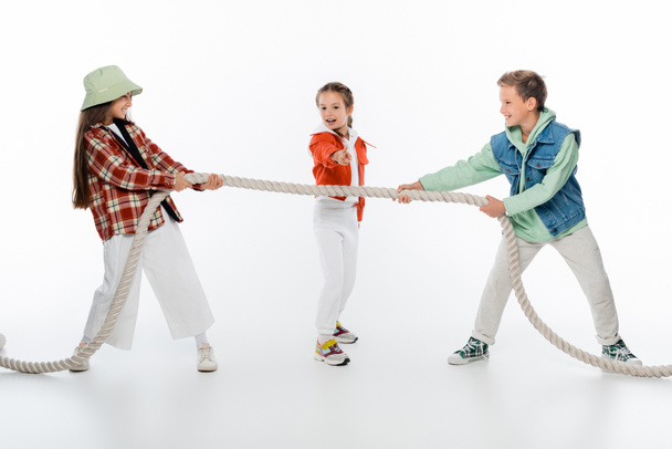 criança pré-adolescente olhando para amigos puxando corda enquanto joga rebocador de jogo de guerra no branco - Foto, Imagem