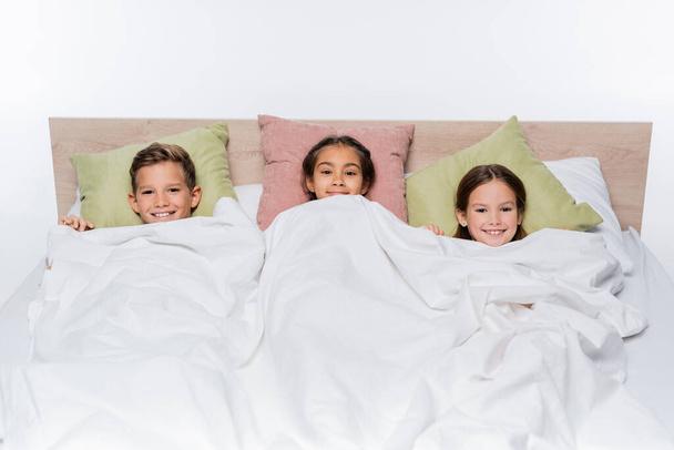 hoge hoek uitzicht van gelukkige kinderen liggen onder deken geïsoleerd op wit - Foto, afbeelding