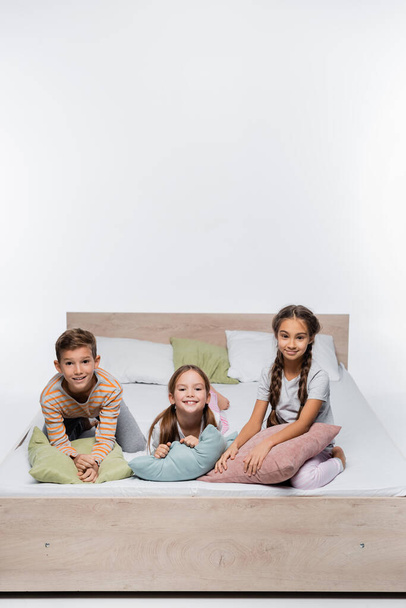 joyful kids sitting on bed with pillows isolated on white - Photo, Image