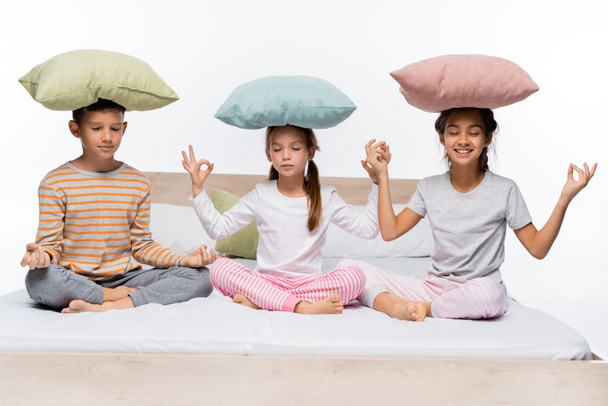 niños felices con almohadas en la cabeza meditando aislados en blanco - Foto, Imagen