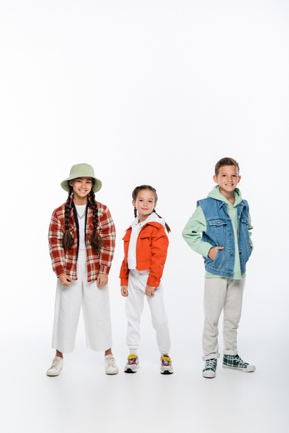 full length of cheerful boy and stylish girls posing on white - Foto, afbeelding