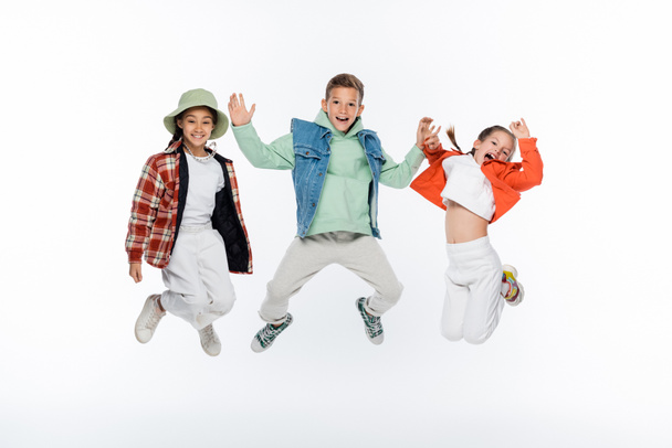full length of stylish kids smiling while jumping on white - 写真・画像