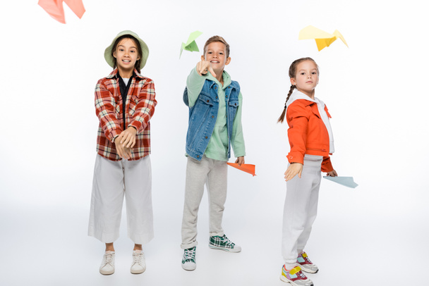 full length of joyful preteen kids throwing paper planes in air on white - Photo, Image