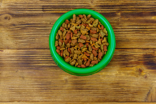 Kuiva ruoka kissalle tai koiralle kulhossa puupohjalla. Lemmikkieläinten ruoka puun pinnalla - Valokuva, kuva