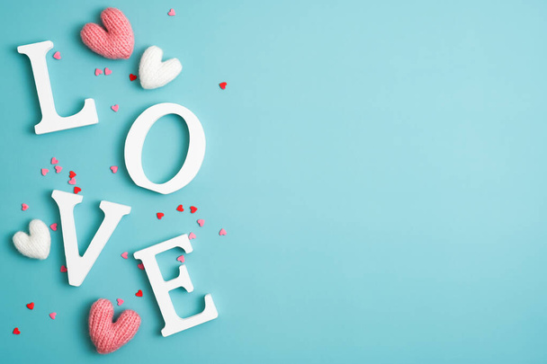 Happy Valentines Day concept. Love word letters and knitted hearts on pastel blue background. Flat lay, top view, copy space. - 写真・画像