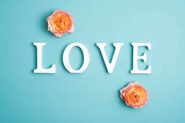 Love word and rose flower buds on pastel blue background. Creative layout, Happy Valentines Day concept. - Fotó, kép