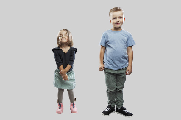 Smiling children are standing. Little girl 3 years old and boy 5 years old. Happy childhood, love and tenderness. Full height. Light gray background. - Photo, image