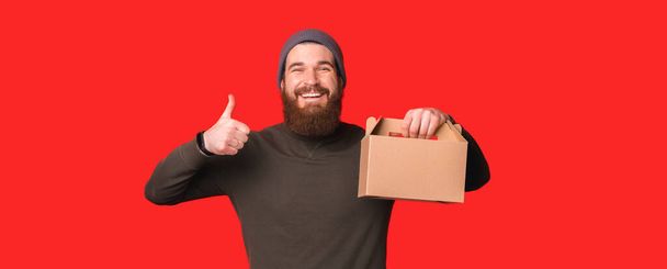 Улыбающийся мужчина показывает большой палец вверх, рекомендуя пакет коробок - Фото, изображение