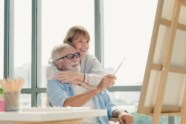 Пожилая пара в повседневной одежде занимаются живописью вместе со счастливыми и романтическими эмоциями в современной комнате. - Фото, изображение