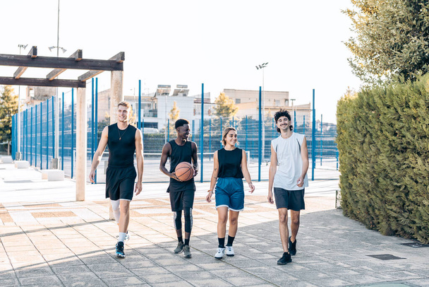 バスケットボールコートの前を歩く異なる民族の4人の友人 - 写真・画像