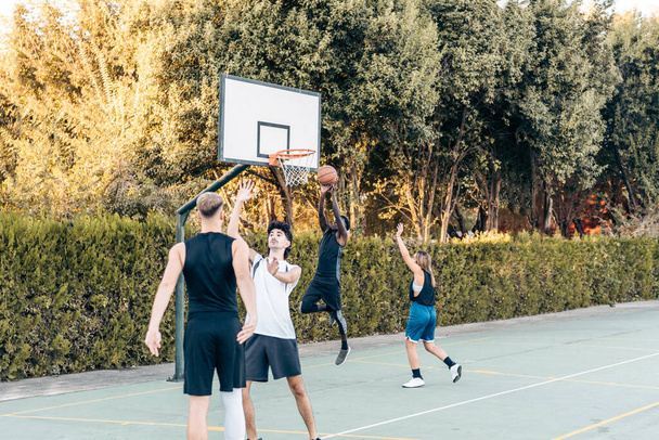 Четверо друзей разных национальностей играют в баскетбол на открытом пространстве на закате - Фото, изображение