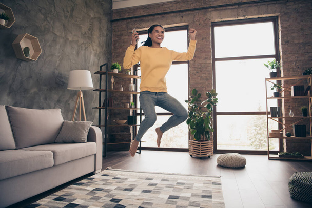 Photo of lucky pretty young woman dressed yellow sweater jumping typinh modern device rising fist indoors home room - Foto, afbeelding