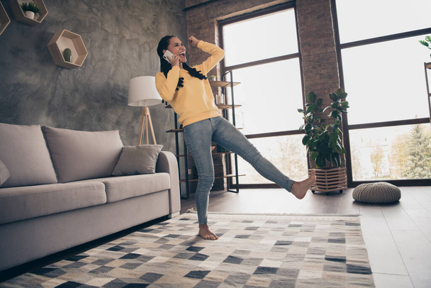 Photo of cute lucky young lady wear yellow pullover rising fist talking modern gadget indoors room home - Foto, afbeelding