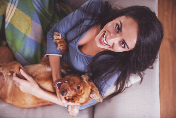 若い女性の平面図は彼女の犬とソファの上で横になっています。. - 写真・画像