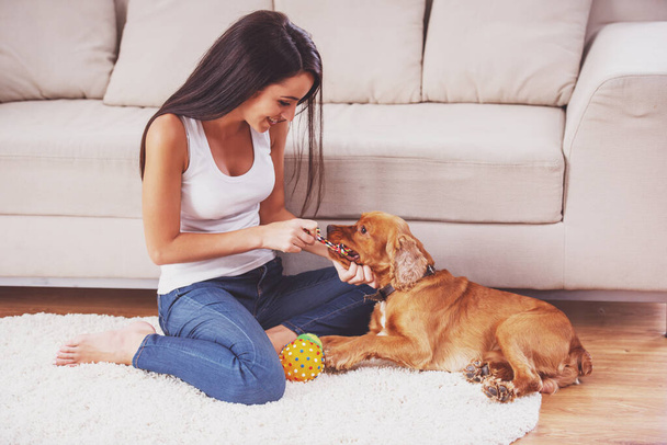 Happy woman is playing with a dog sitting on the floor at home. - Foto, Imagen
