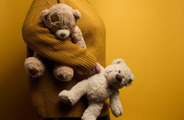Frau in orangefarbenem Strickpullover umarmt niedlichen braunen Teddybär. Das Konzept von Einsamkeit und Traurigkeit, Depression - Foto, Bild