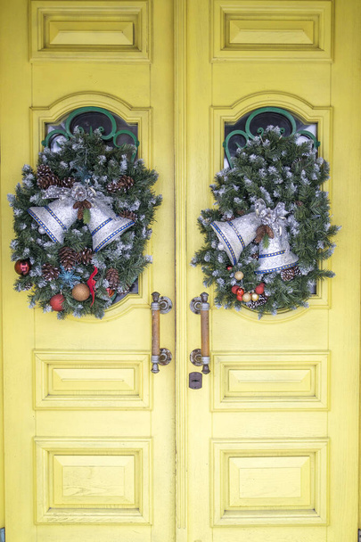 Christmas wreath of fir branches with decorations hanging on the yellow door of the house - Фото, изображение
