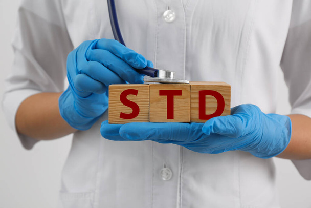 Doctor holding wooden cubes with abbreviation STD and stethoscope on white background, closeup - Foto, Imagem