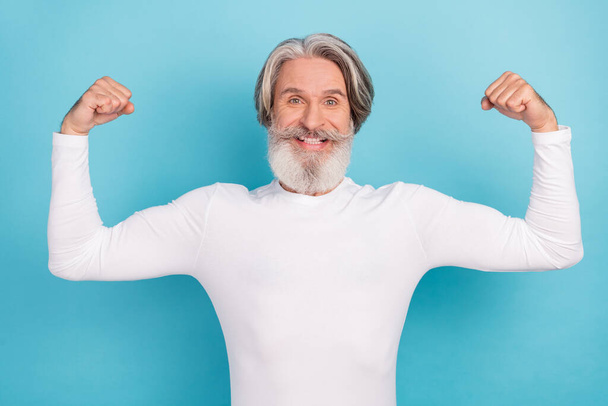 Portrait of attractive cheerful proud grey-haired man demonstrating muscles isolated over bright blue color background - Foto, Bild