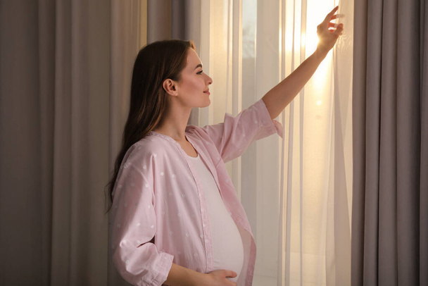 Nuori raskaana oleva nainen lähellä ikkunaa kotona - Valokuva, kuva