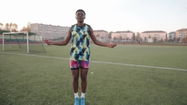Chica negra activa en un brillante chándal entrena en el campo de fútbol y saltar la cuerda. Concepto de deporte y estilo de vida saludable - Metraje, vídeo