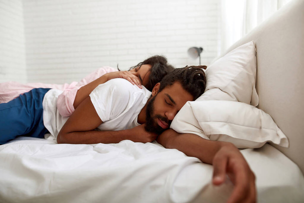 Black couple sleeping under blanket on bed at home - Foto, Imagen