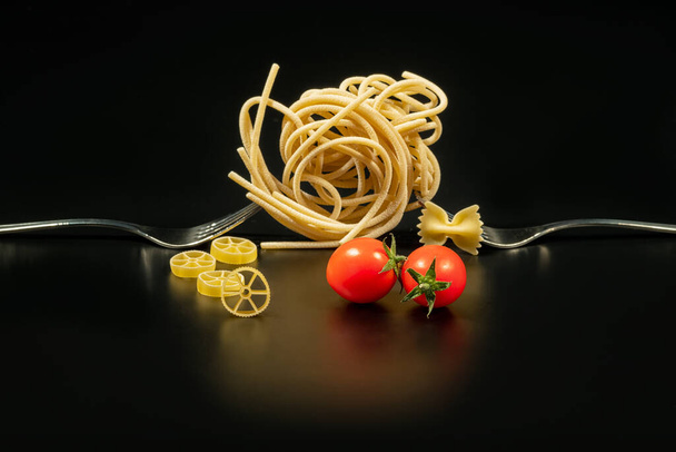 Creative still life photo of two forks with raw pasta on black background - Fotó, kép