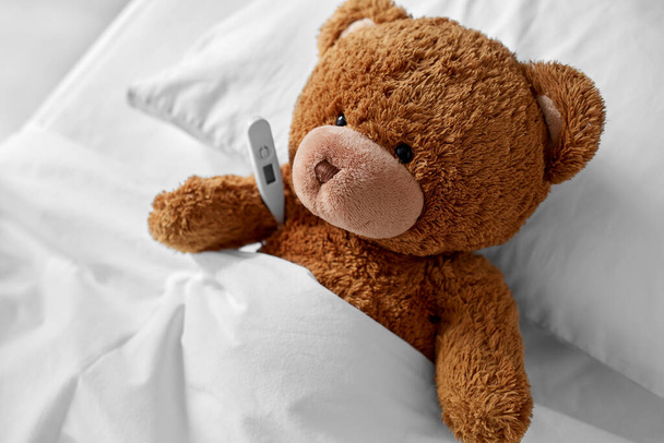 ill teddy bear toy head with thermometer in bed - Valokuva, kuva