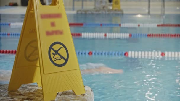 Προσοχή σημάδι κοντά στην πισίνα - μην βουτήξετε στο νερό - ένας περαστικός κολυμβητής σε φόντο - Πλάνα, βίντεο