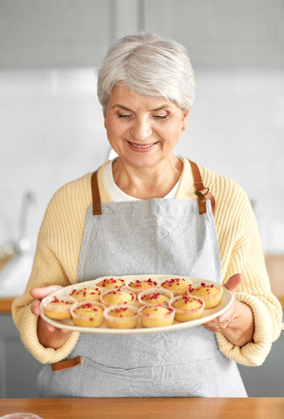 woman holding plate with cupcakes on kitchen - Zdjęcie, obraz