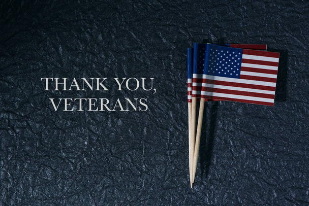 hoge hoek uitzicht op een aantal vlaggen van de Verenigde Staten van Amerika, bevestigd aan houten palen, op een donker oppervlak en de dank u veteranen - Foto, afbeelding