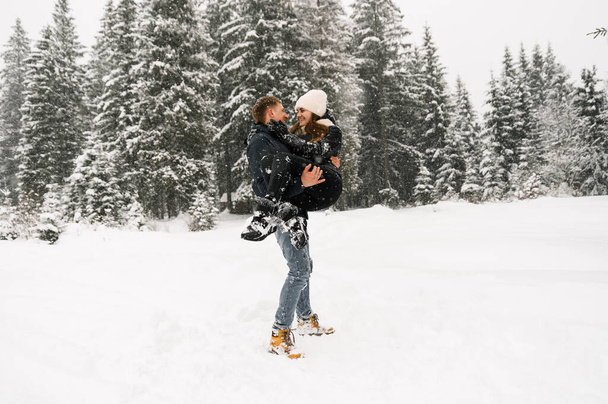 Kochająca para przytulająca się na zimowym spacerze. Młoda rodzina bawiąca się w mroźnym lesie. Romantyczna randka zimą. Miłosierdzie zimowe - Zdjęcie, obraz