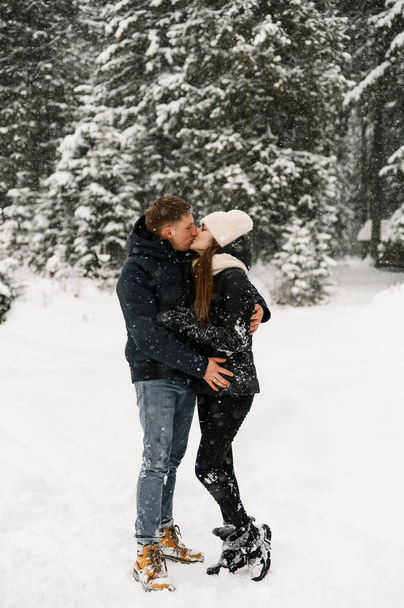 Loving couple cuddling on a winter walk. Young family having fun in the frosty forest. Romantic date in winter time. Winter lovestory - Zdjęcie, obraz