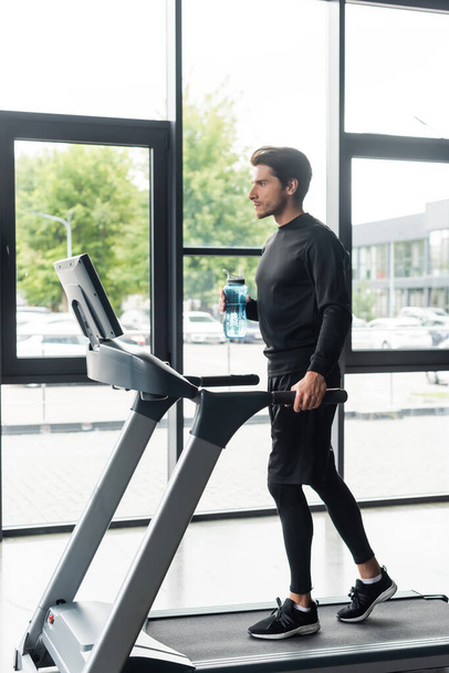 Side view of man holding sports bottle while running on treadmill in gym  - Fotoğraf, Görsel