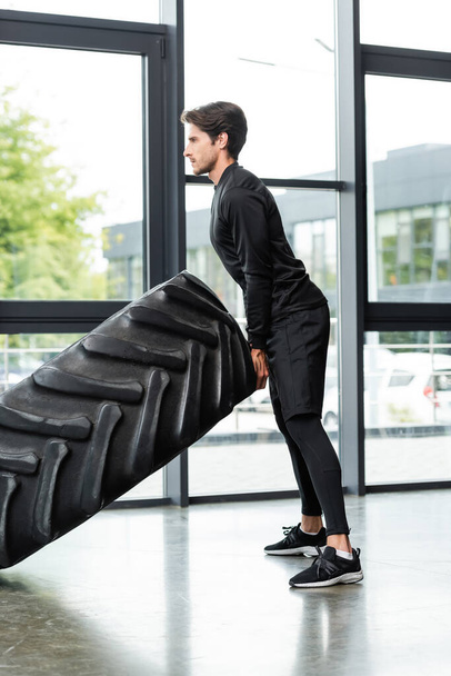 Side view of sportswoman training while lifting tire in sports center  - Fotoğraf, Görsel