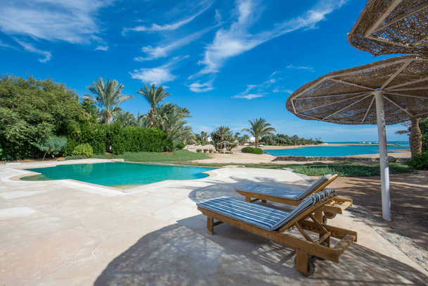Luxus-Villa in tropischer Sommerferienanlage mit Pool und Liegestühlen mit Meerblick - Foto, Bild