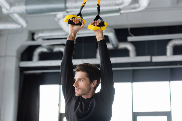 Sportsman working out with suspension straps in sports center  - Foto, imagen