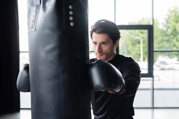 Sportsman in boxing gloves training with punching bag in sports center  - 写真・画像