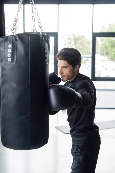 Sportsman dans l'entraînement de vêtements de sport avec sac de boxe dans la salle de gym  - Photo, image