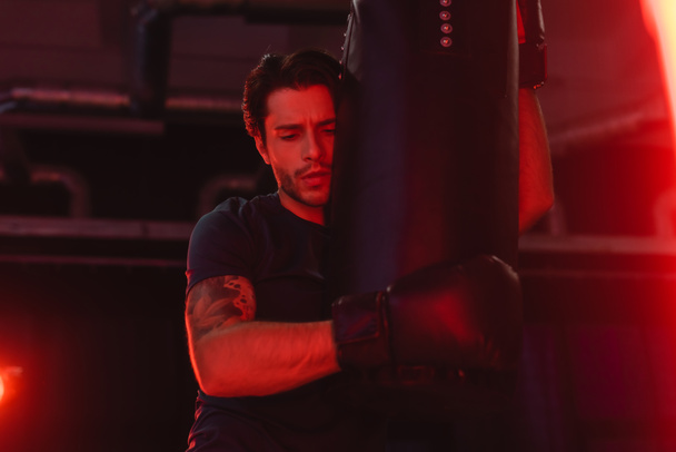 Sportsman hugging punching bag in gym with red light  - Photo, image