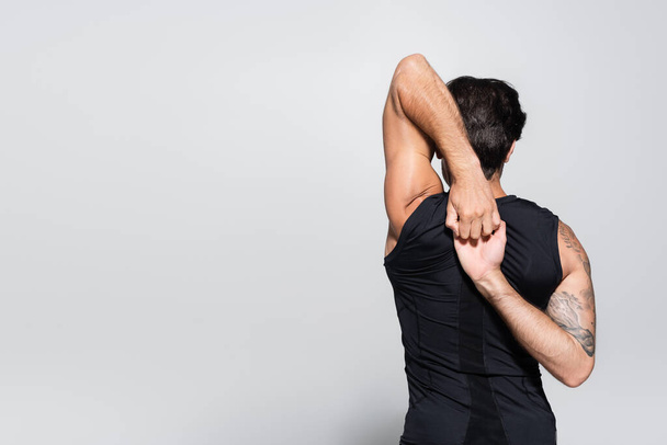 Back view of tattooed sportsman stretching arms on grey background  - Fotografie, Obrázek