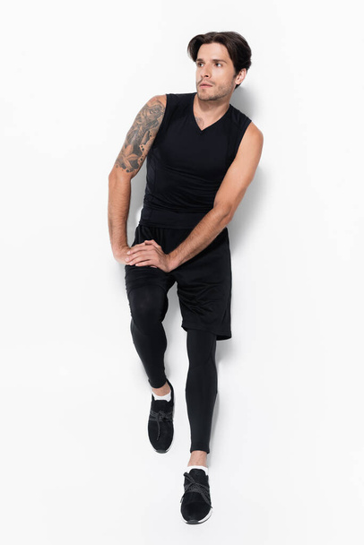 Longitud completa del hombre tatuado en ropa deportiva de pie sobre fondo gris - Foto, imagen
