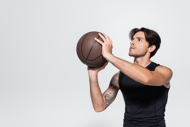 Deportista sosteniendo pelota de baloncesto mientras mira hacia otro lado aislado en gris  - Foto, Imagen