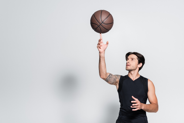Tattooed sportsman holding basketball ball on finger on grey background - 写真・画像