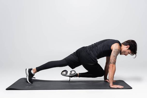 Side view of sportsman working out on black fitness mat on grey background - Fotoğraf, Görsel