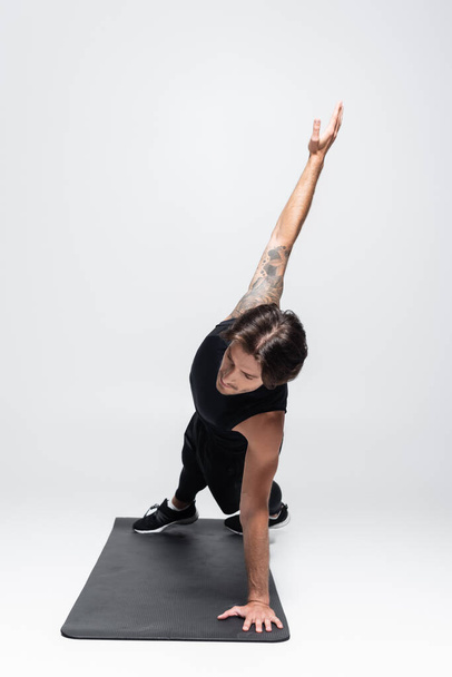 Deportista tatuado haciendo tablón lateral en alfombra de fitness sobre fondo gris - Foto, Imagen