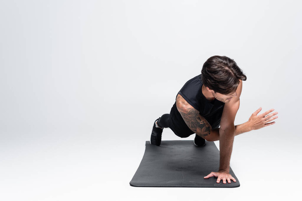 Athletic sportsman in black sportswear doing plank on fitness mat on grey background - Foto, Imagem